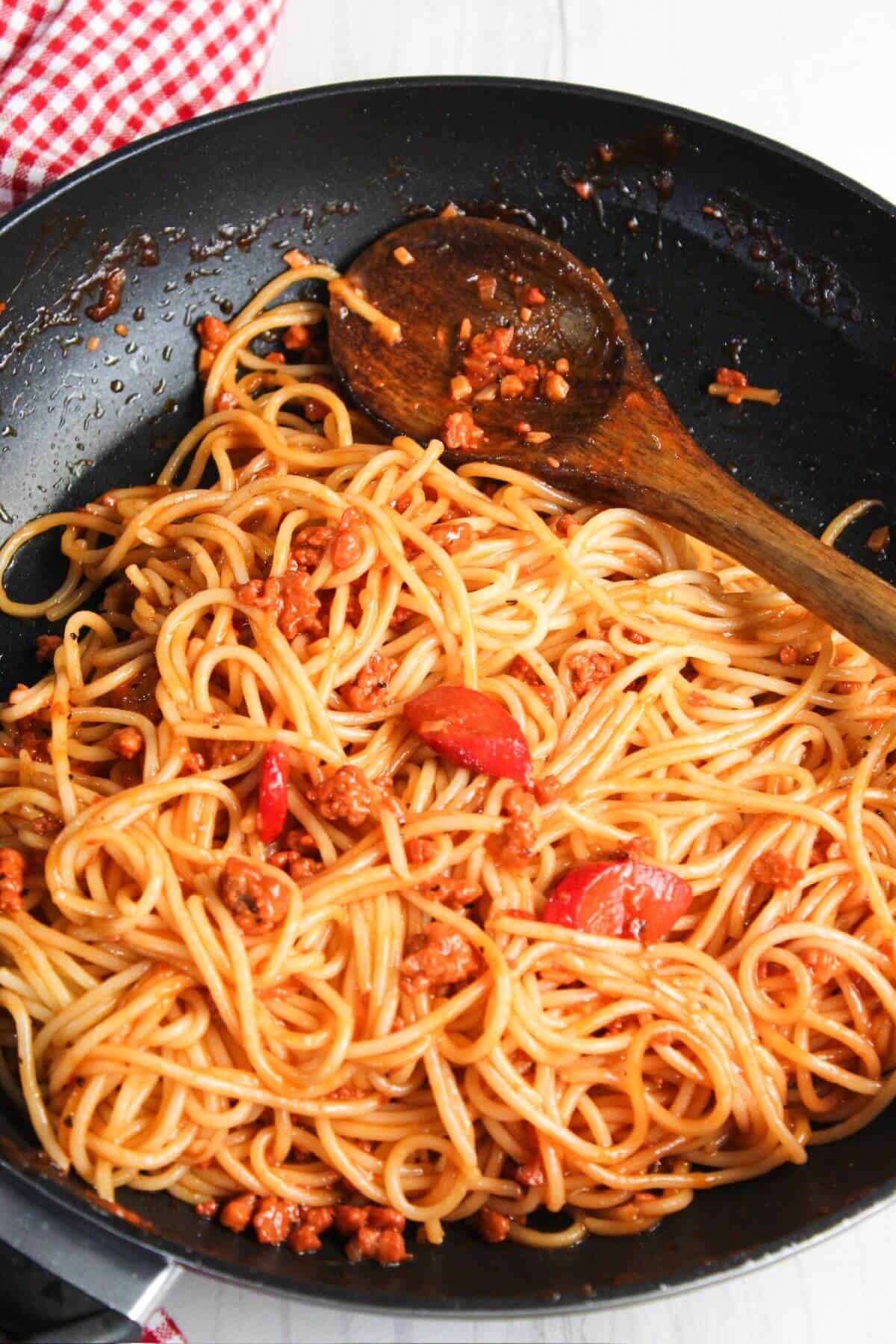 Spaghetti with meat and tomatoes in a frying pan.