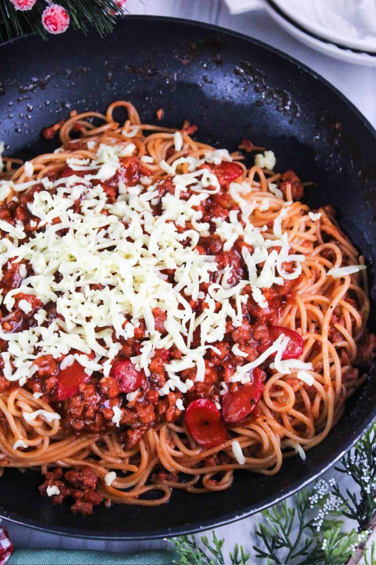 Filipino spaghetti and meat sauce topped with cheese in a frying pan.