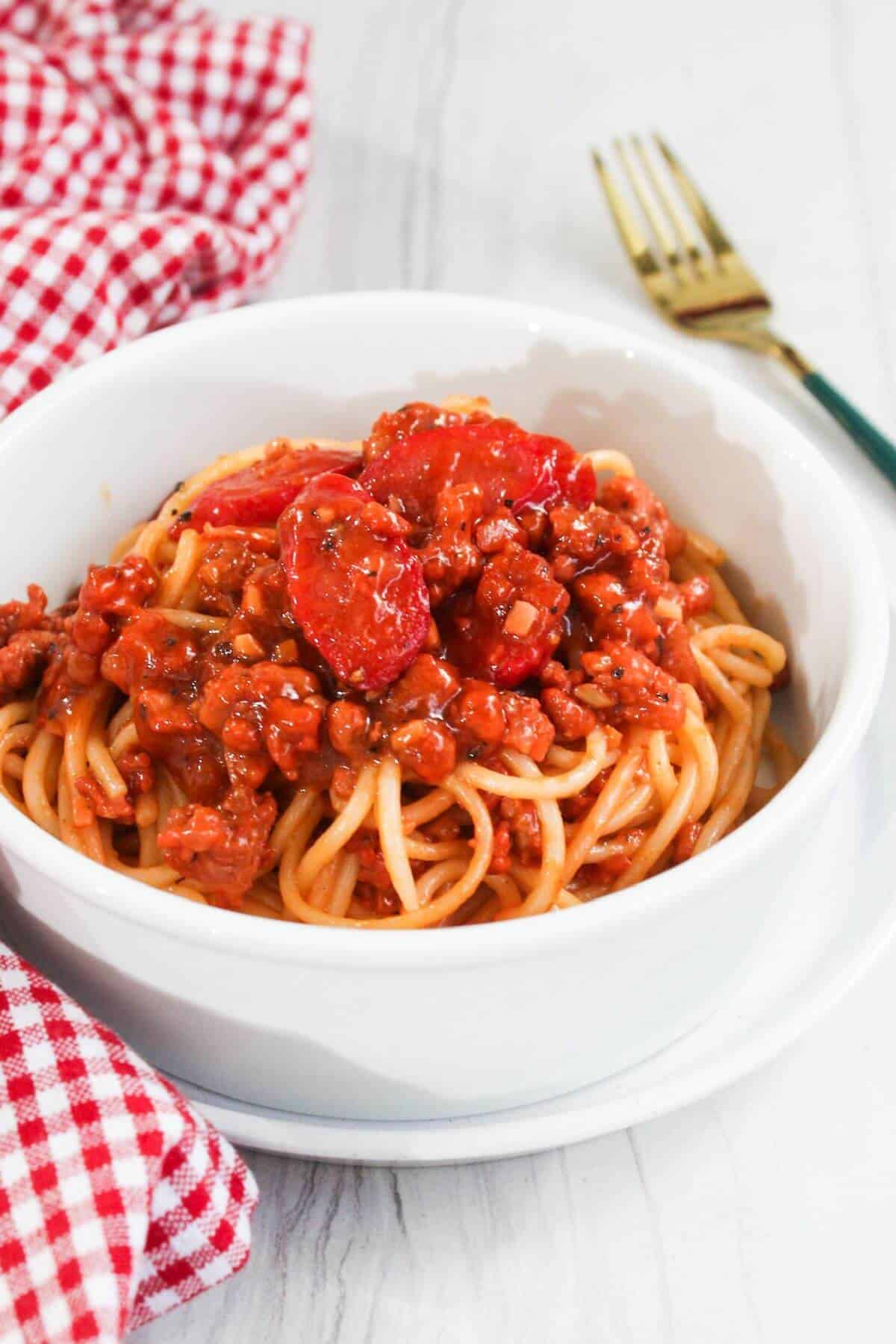 A bowl of spaghetti with meat sauce and tomatoes.
