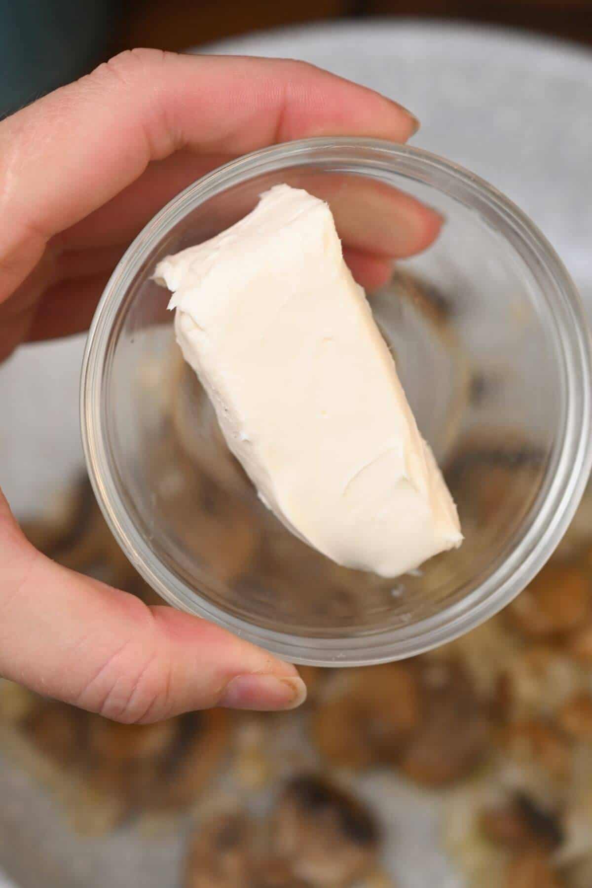 A person holding a piece of butter in a glass bowl.