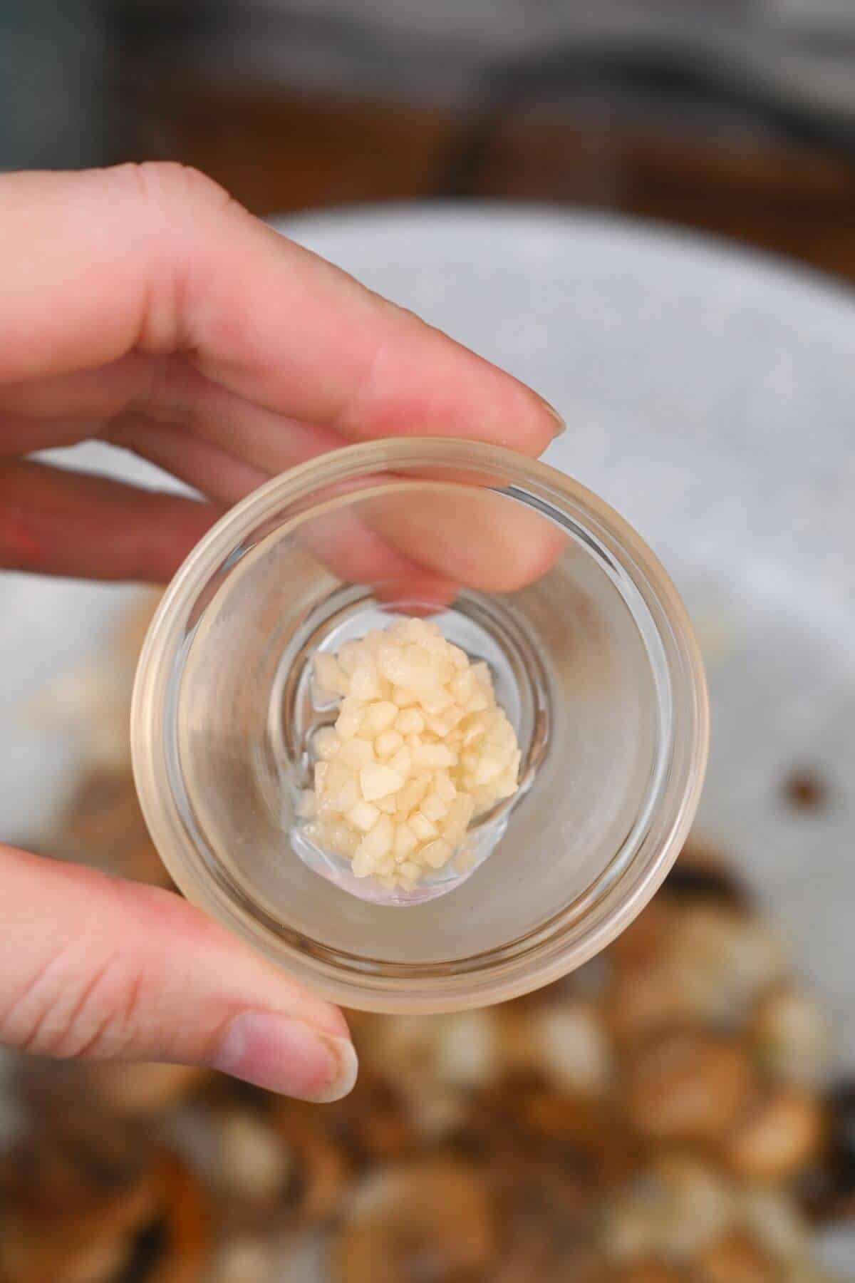 A person holding a glass bowl with minced garlic in it.