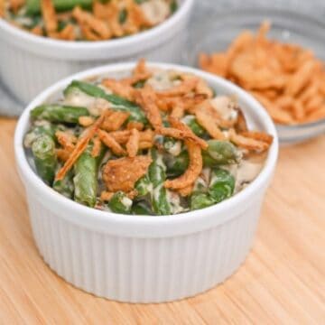 Two bowls of green bean casserole on a cutting board.