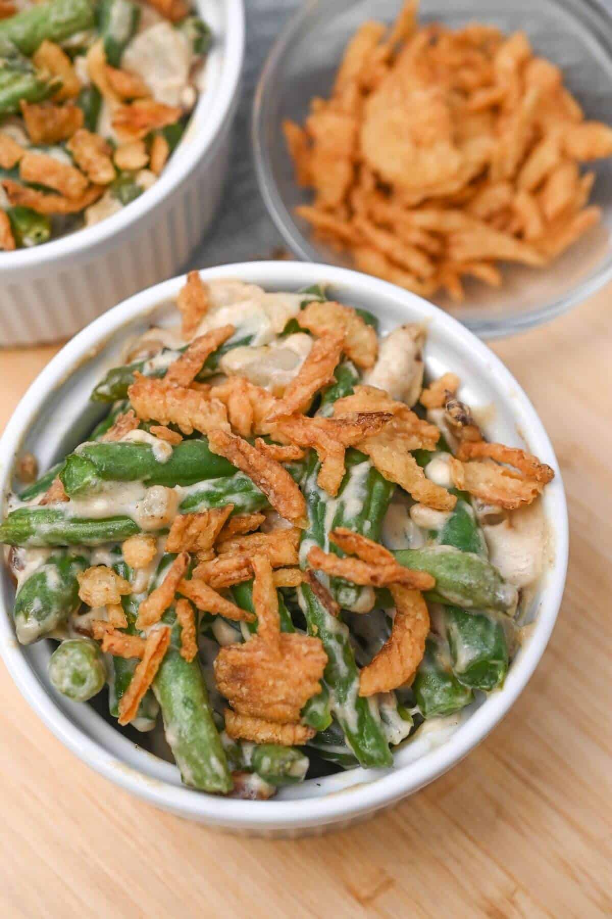 Two bowls of green bean casserole on a wooden table.