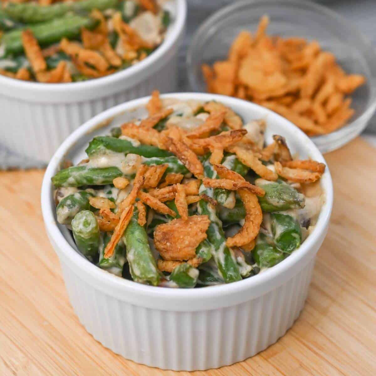 Two bowls of green bean casserole on a cutting board.