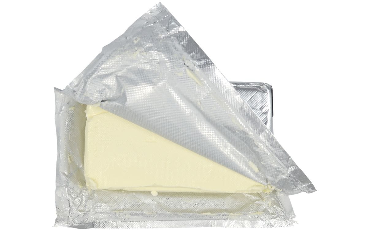 A piece of cream cheese wrapped in foil on a white background.