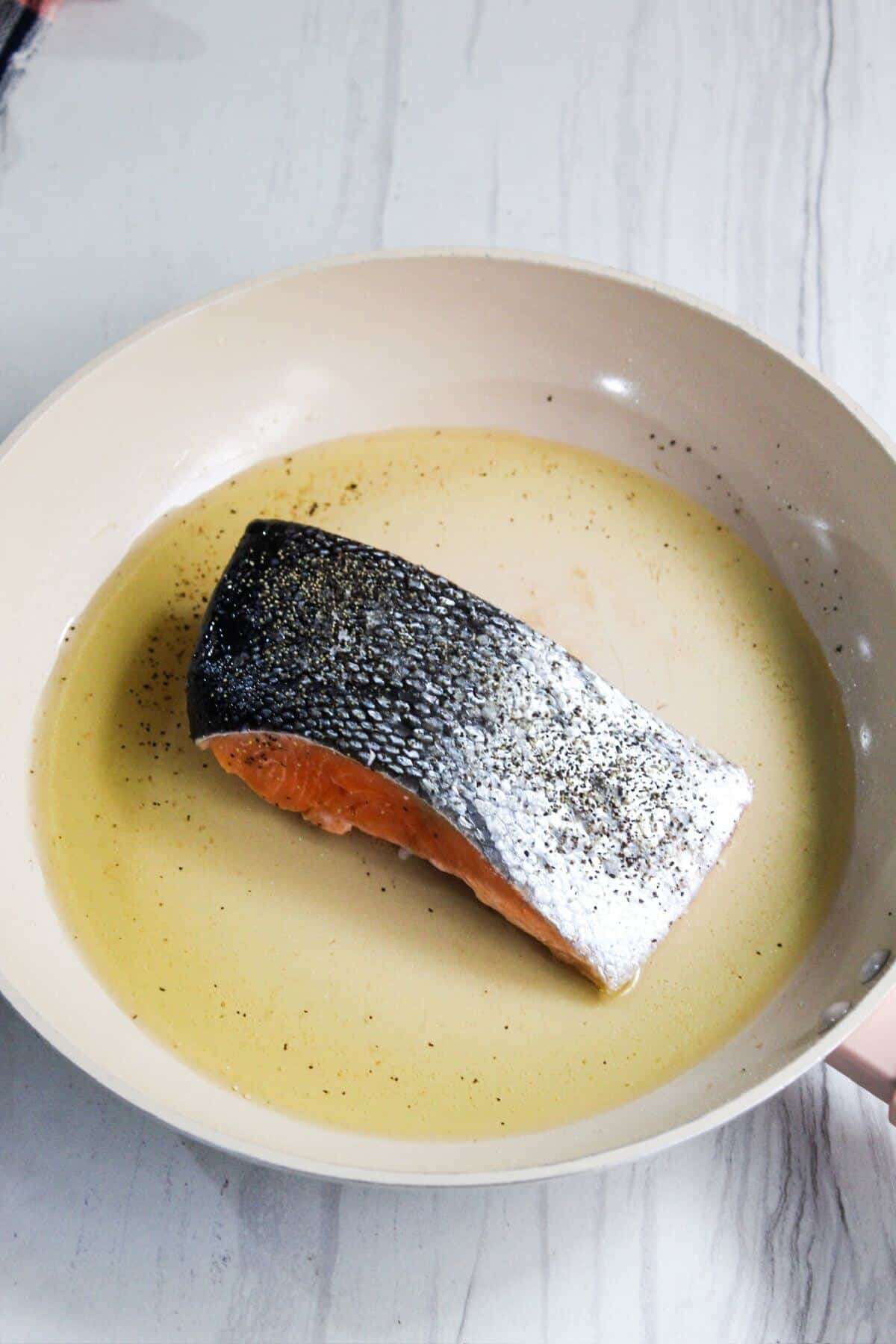 A salmon fillet in a frying pan with oil.
