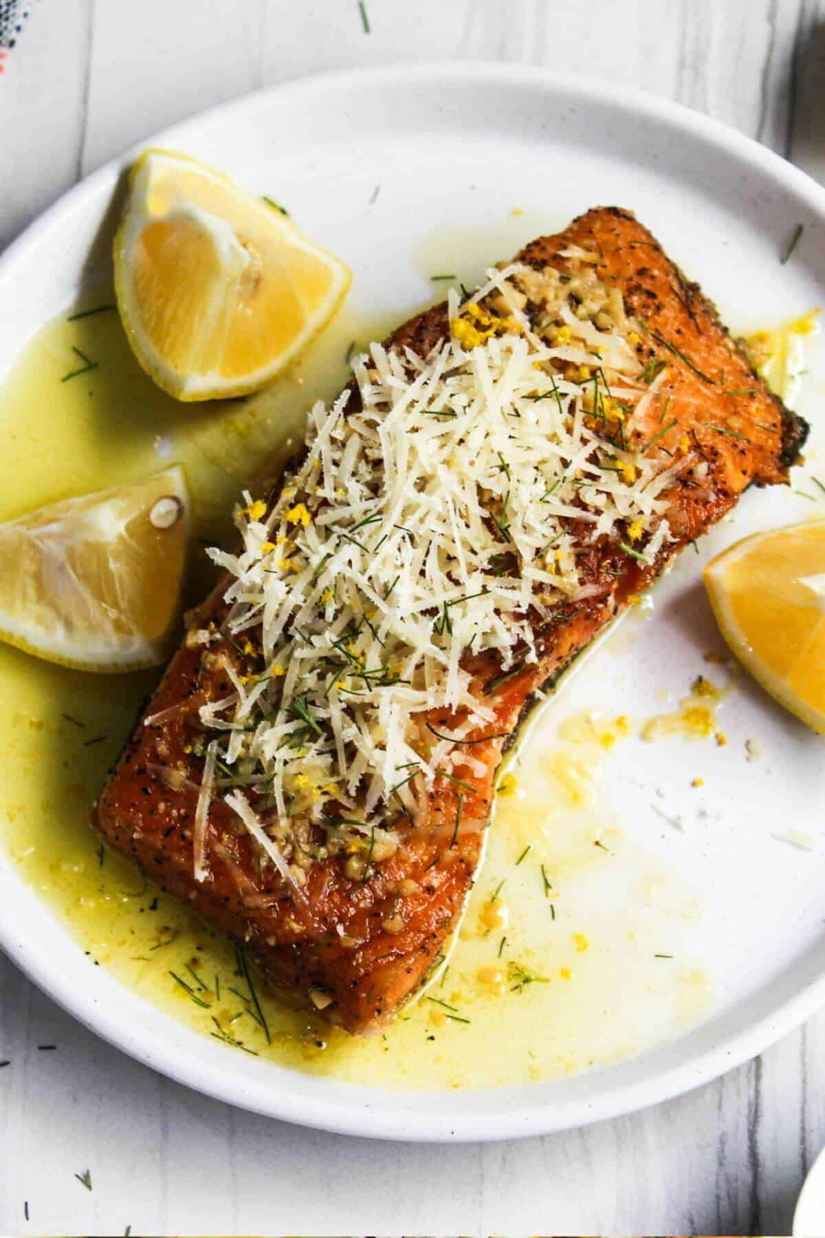 Salmon with lemon and parmesan on a white plate.