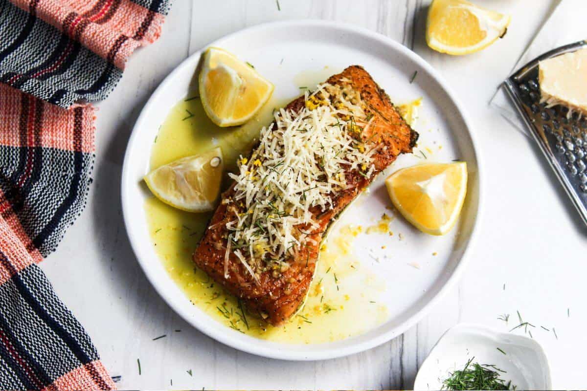 A plate of salmon on a white plate with lemon slices on it.