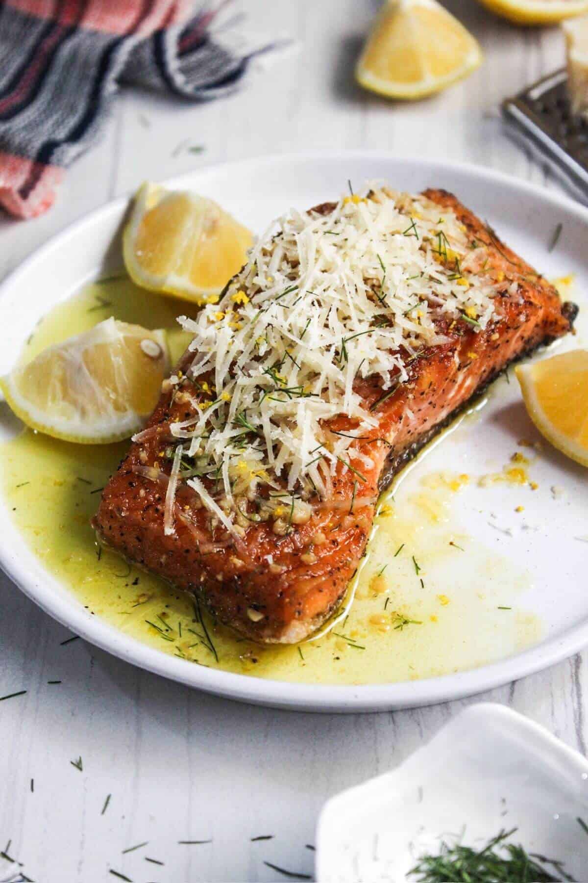 Salmon with lemon butter sauce and parmesan on a white plate.