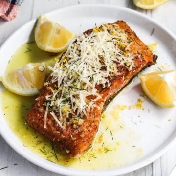 Salmon with lemon butter sauce and parmesan on a white plate.