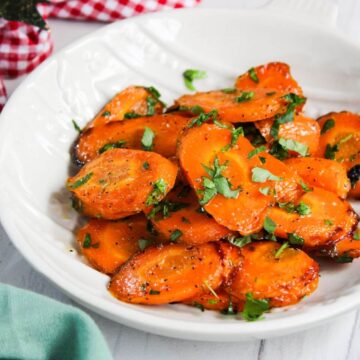 Maple-glazed carrots in a white bowl with herbs.
