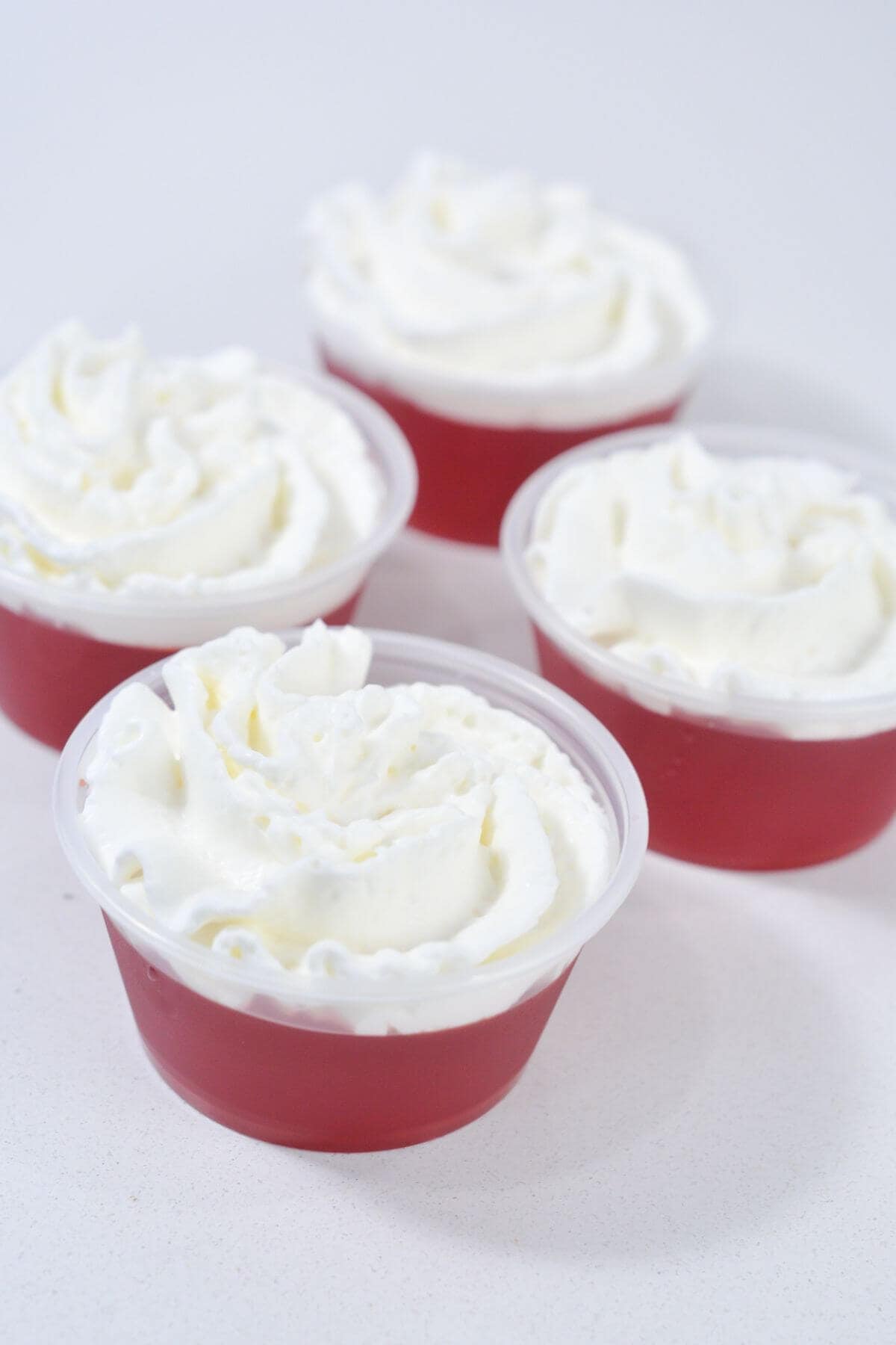 Four red gelatin cups with whipped cream.