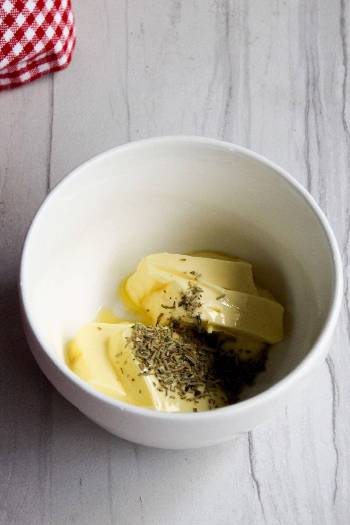 Butter in a white bowl with dried rosemary.