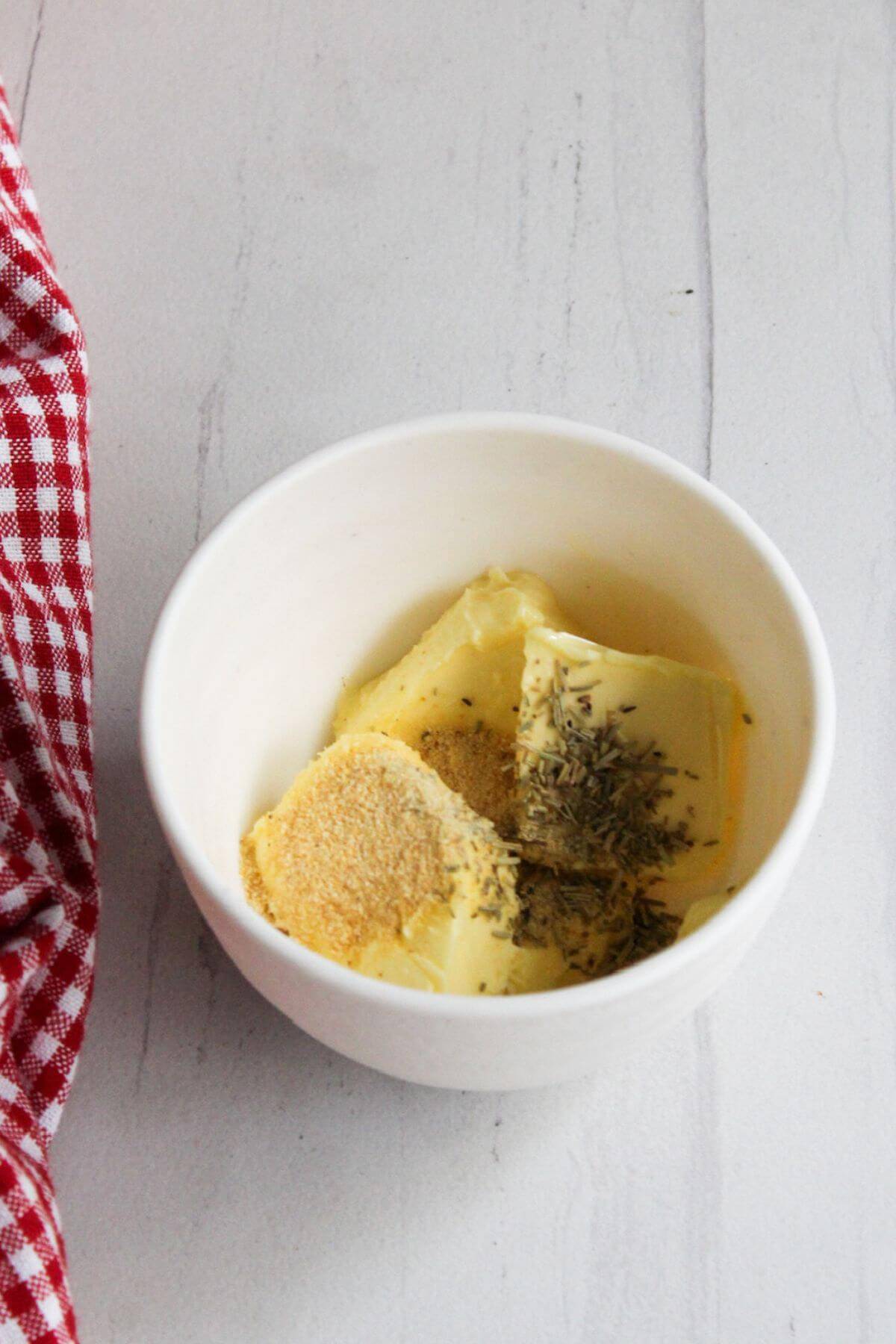 Butter and seasonings in a bowl next to a red and white checkered napkin.