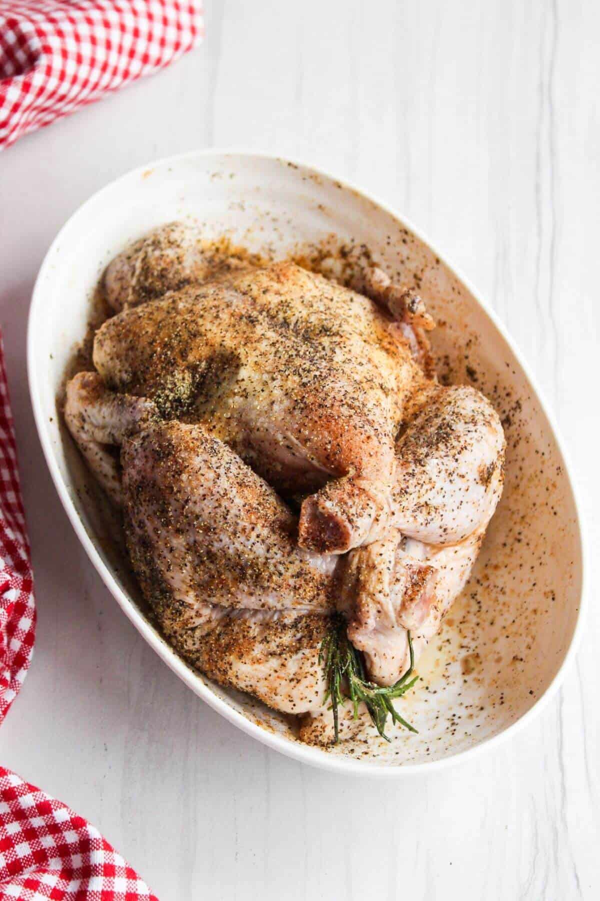 Whole chicken rubbed with seasoning in a white bowl on a white table.
