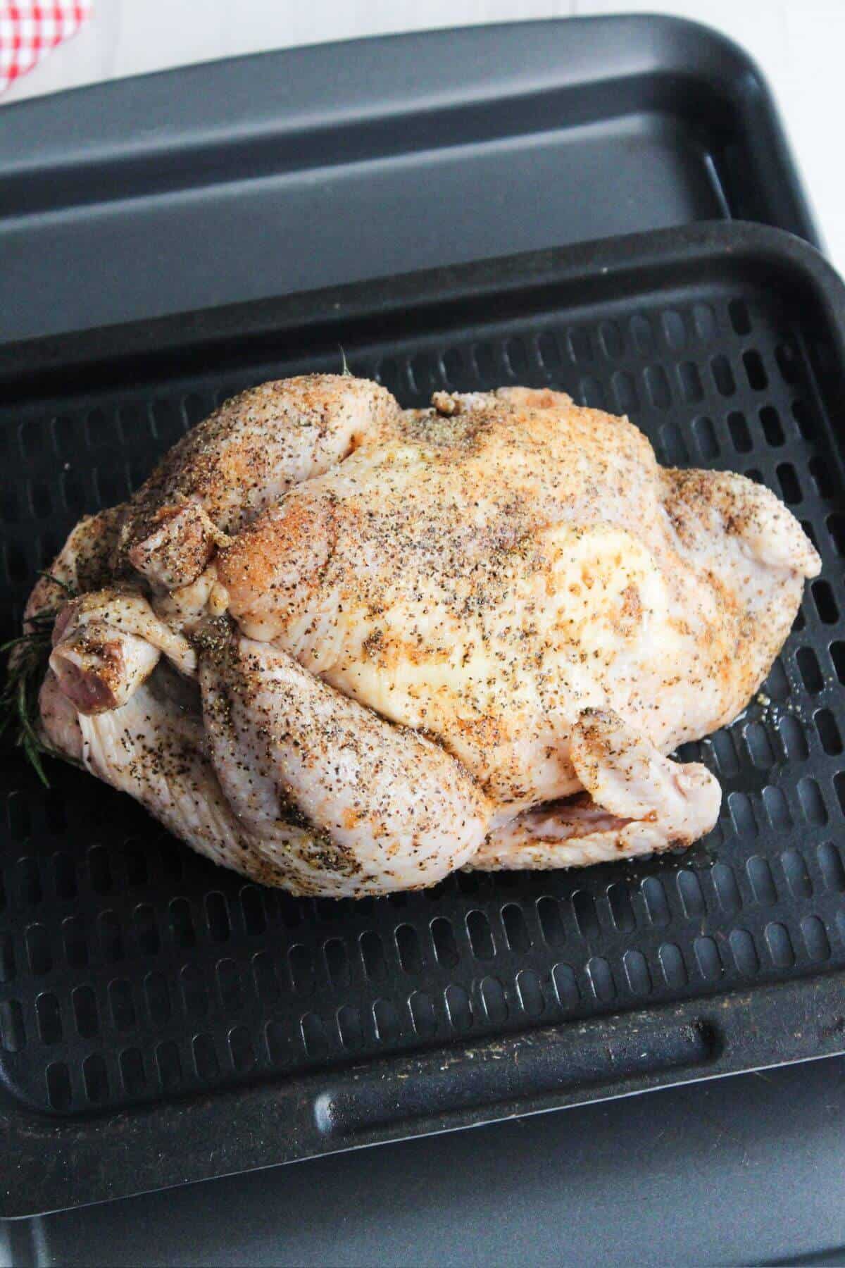 A whole chicken is sitting on an air fryer tray.