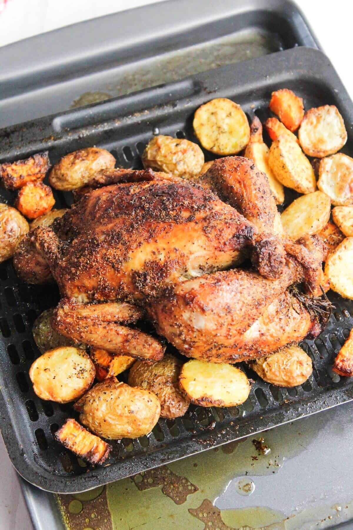 Whole chicken with roasted potatoes and carrots on an air fryer tray.