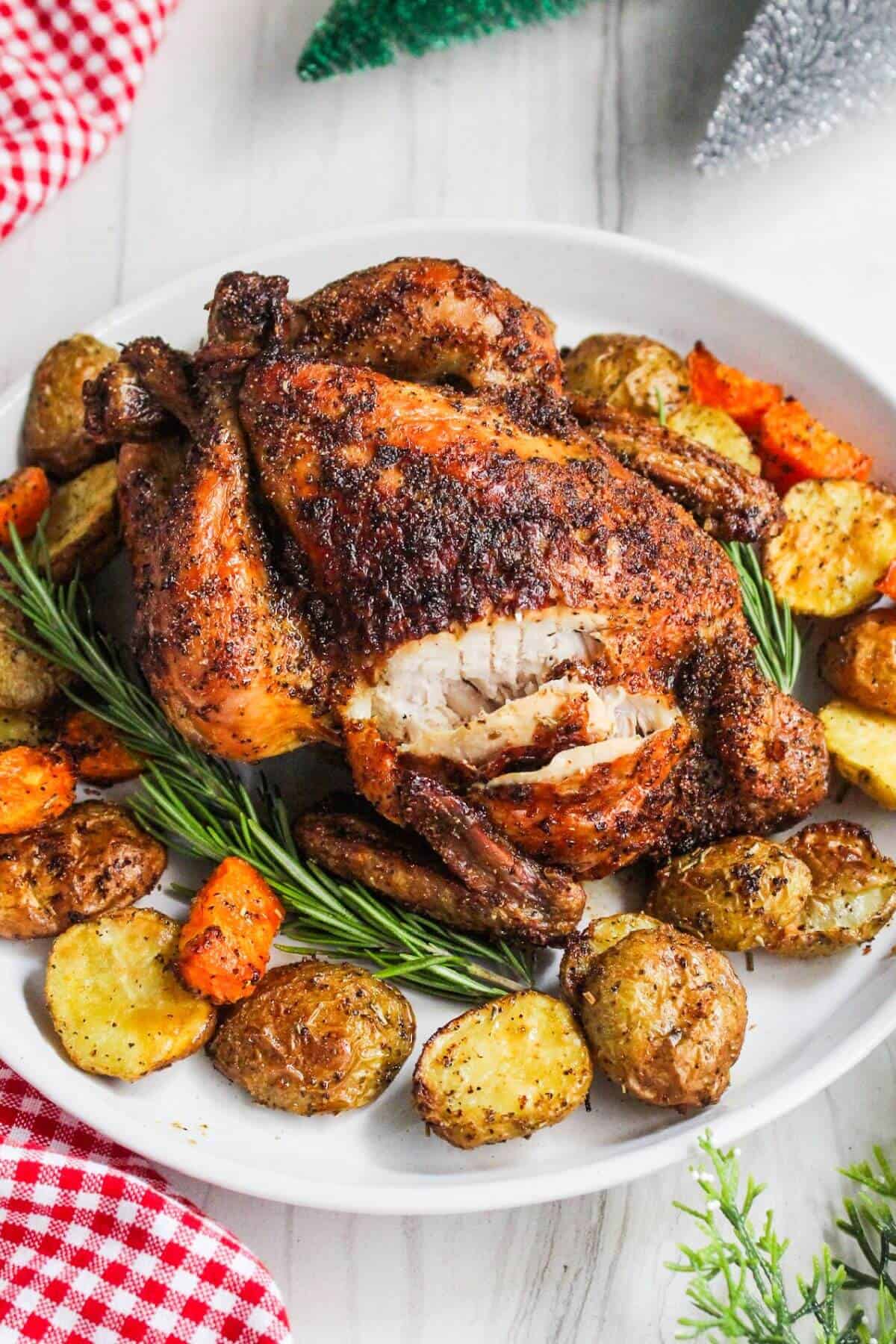 Whole roasted chicken with potatoes and carrots on a white plate.