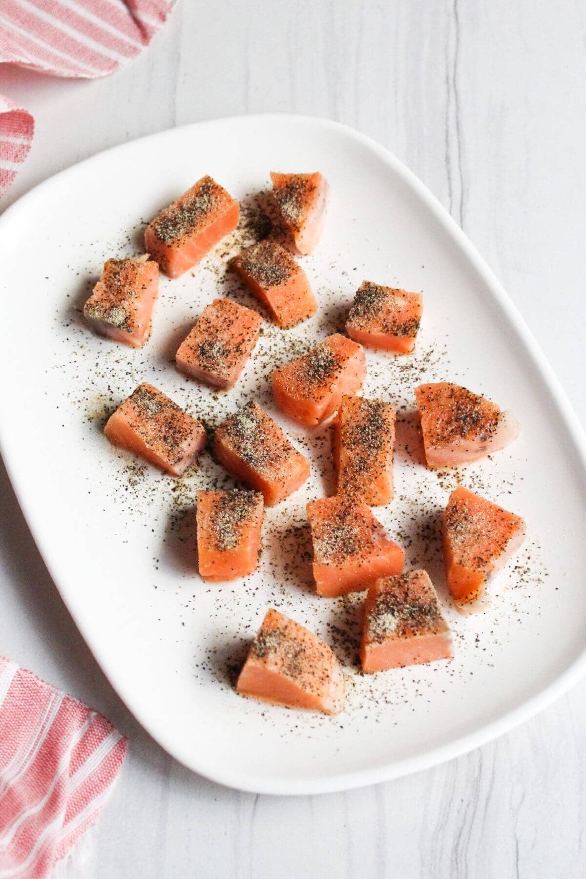 Seasoned salmon cubes on a white plate.