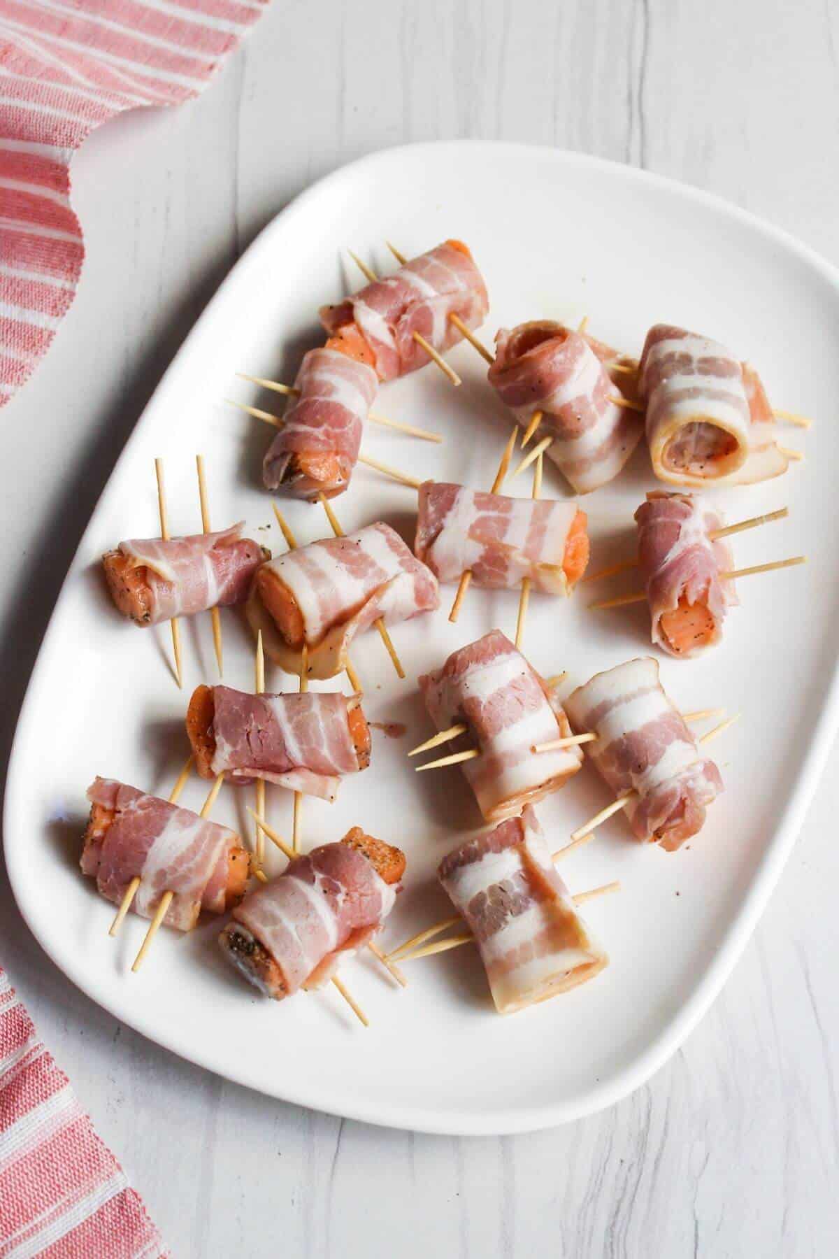 Bacon wrapped salmon bites with toothpicks inserted on a white plate.