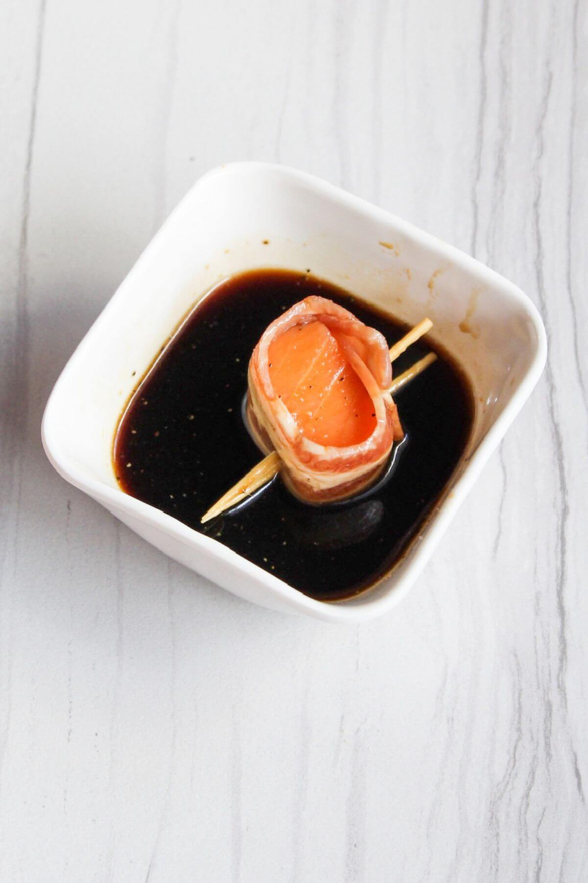 Dipping bacon wrapped salmon in soy sauce mixture.