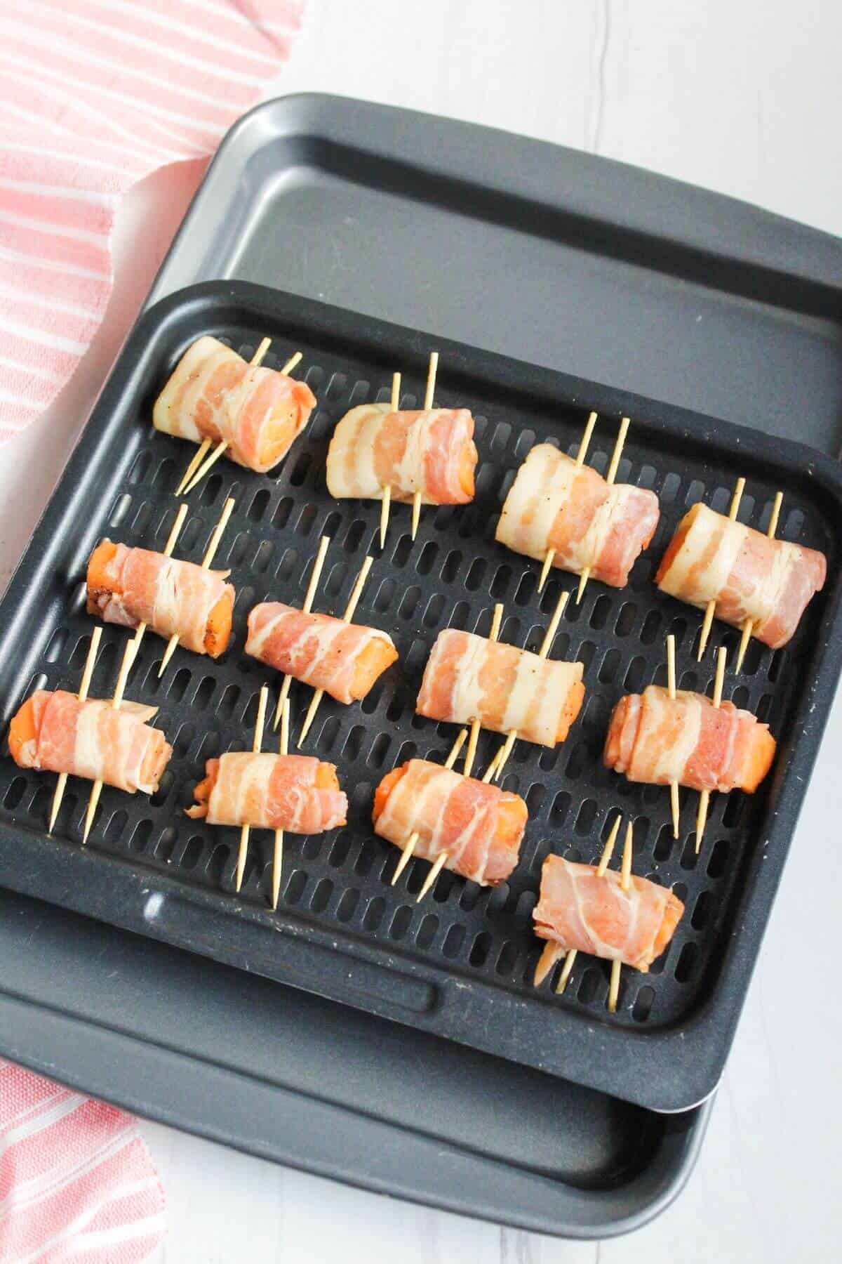 Bacon wrapped salmon bites on toothpicks arranged on an air fryer tray.