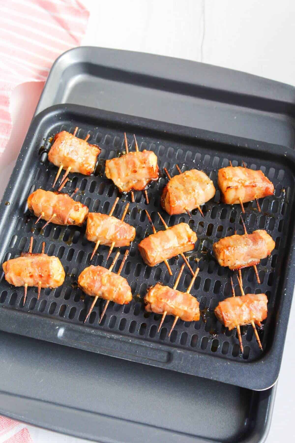 Bacon-wrapped salmon on an air fryer tray with toothpicks.