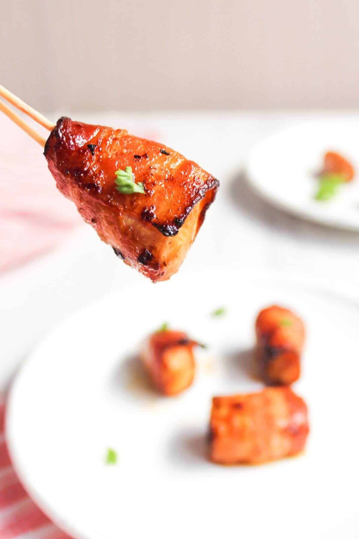 A person is holding a piece of bacon-wrapped salmon on a stick.