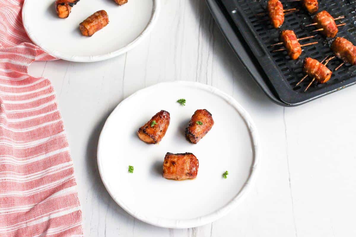 Bacon wrapped salmon bites on small round plates with air fryer tray in back.