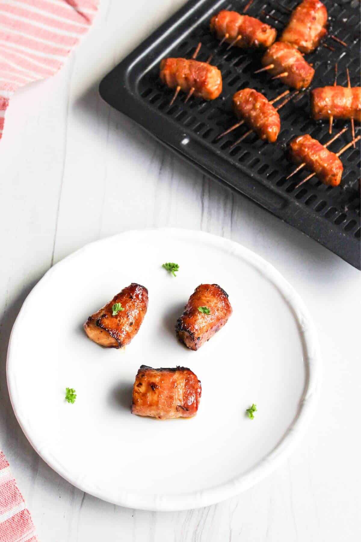 A plate of bacon-wrapped salmon bites with air fryer tray in back.