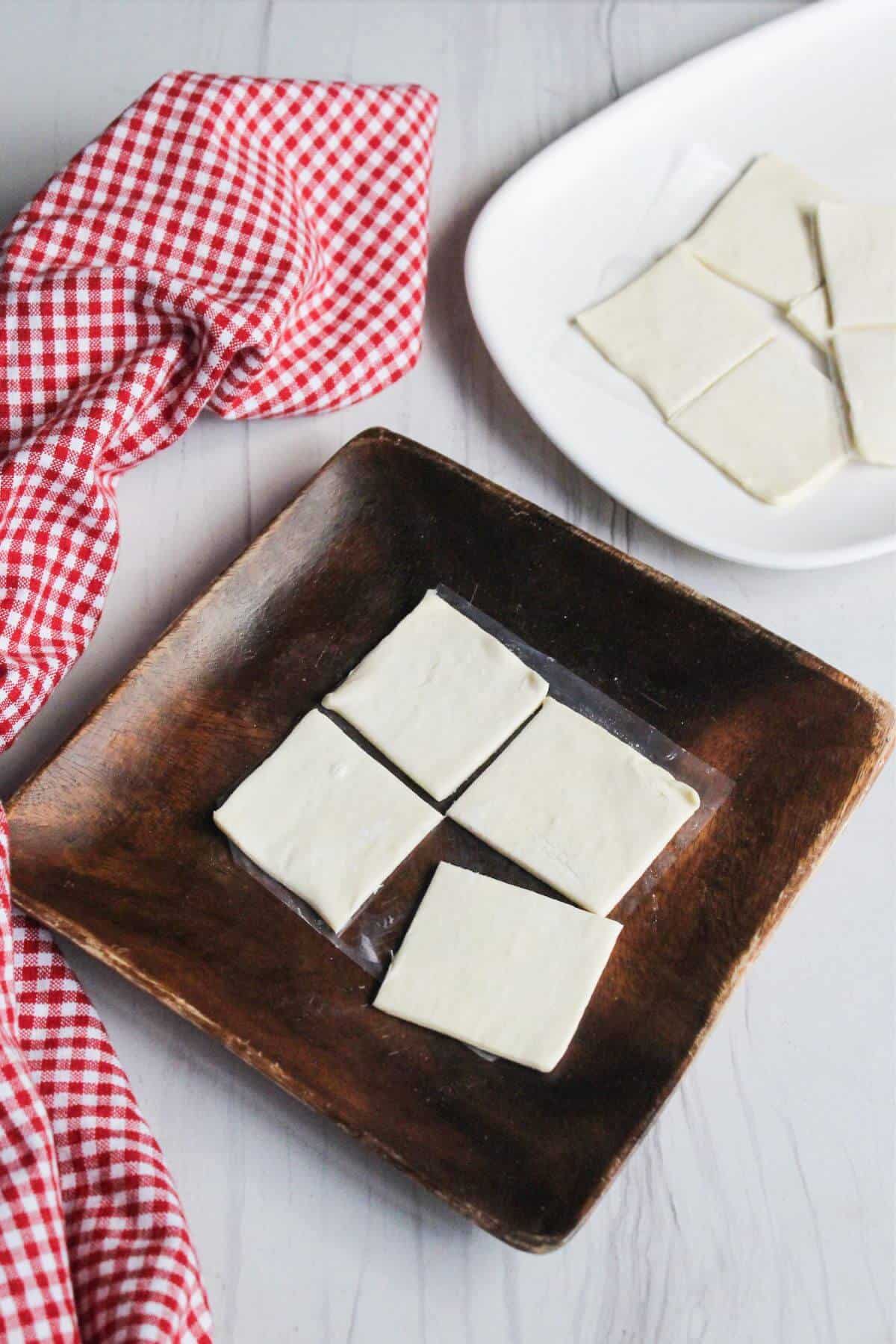 A plate with puff pastry squares and a red and white checkered napkin.