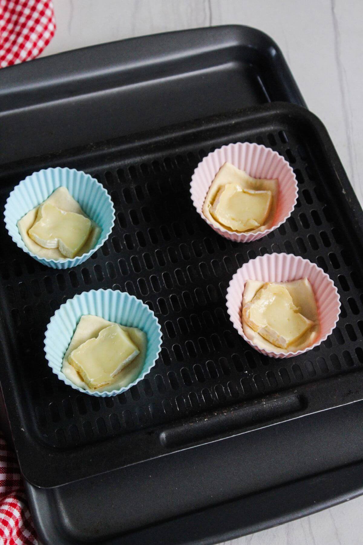 A baking sheet of muffin cups with puff pastry and brie.