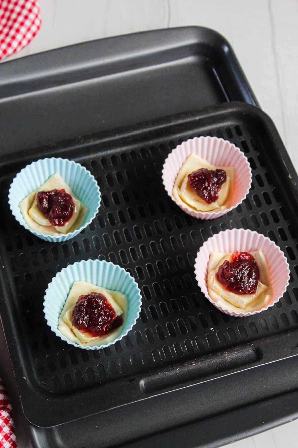 A baking sheet with silicone muffin cups with pastry, brie, and cranberry sauce in them.
