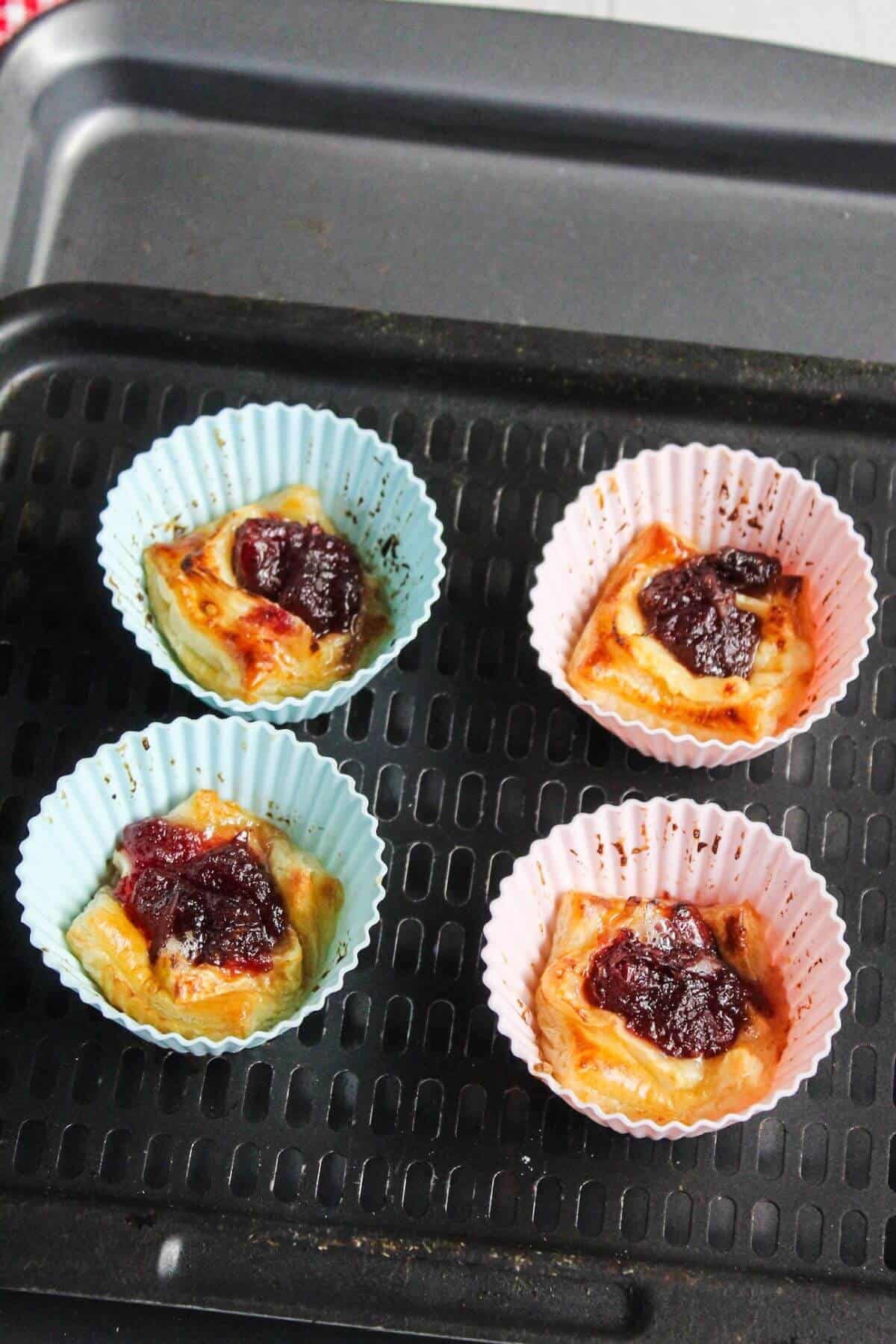 A baking tray of brie and cranberry puff pastry bites in silicone muffin cups.