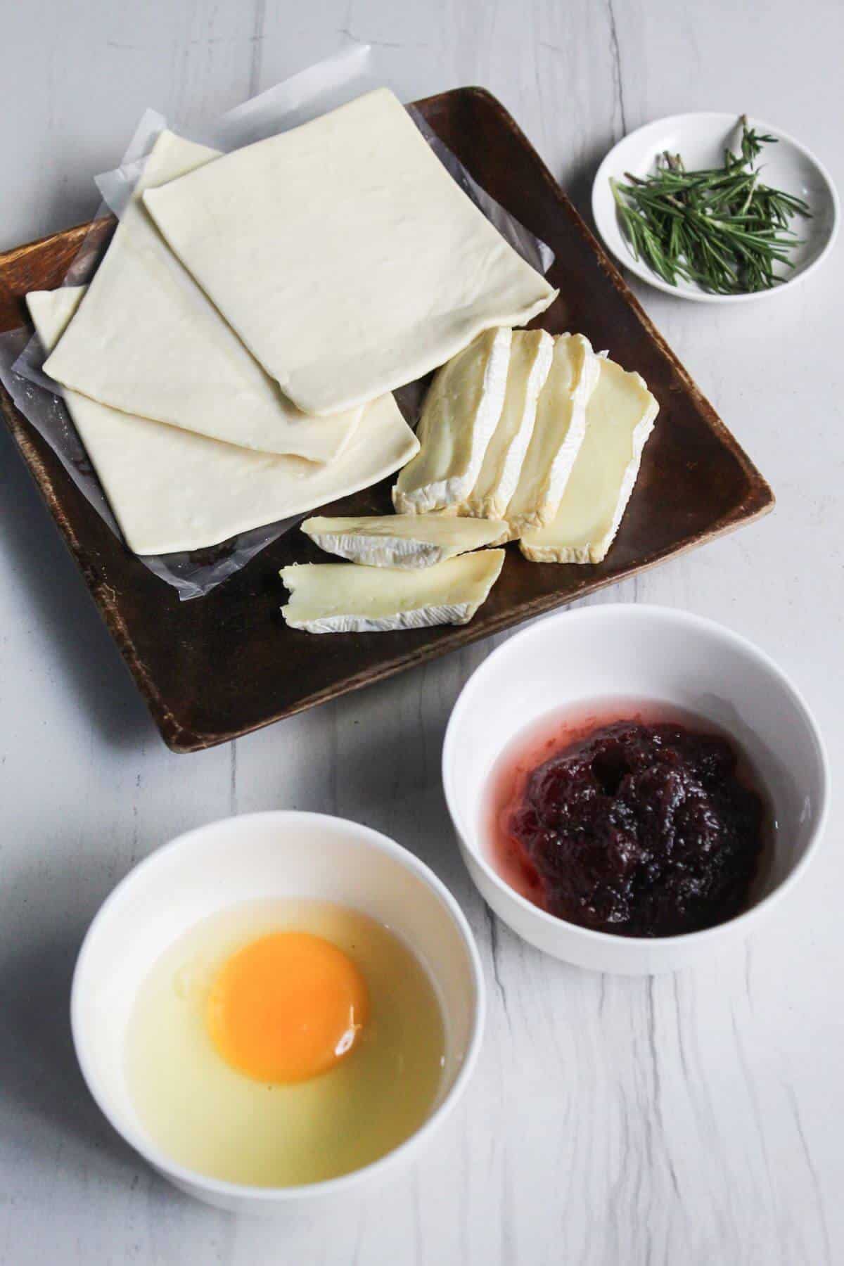 A plate with puff pastry sheets, cheese, egg, and cranberry sauce.