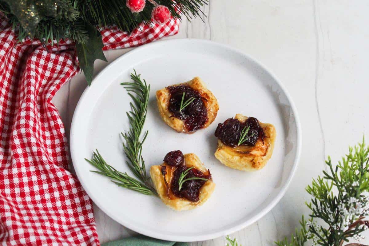 Tarts with cranberries and rosemary on a white plate.
