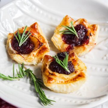 Cranberry mini pastries with rosemary sprigs on a white plate.