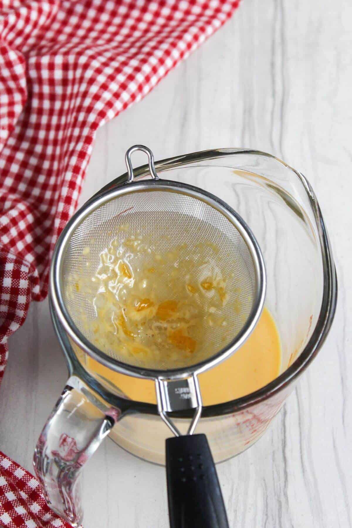 A glass bowl with a strainer over it, used for straining egg yolk mixture for leche flan.