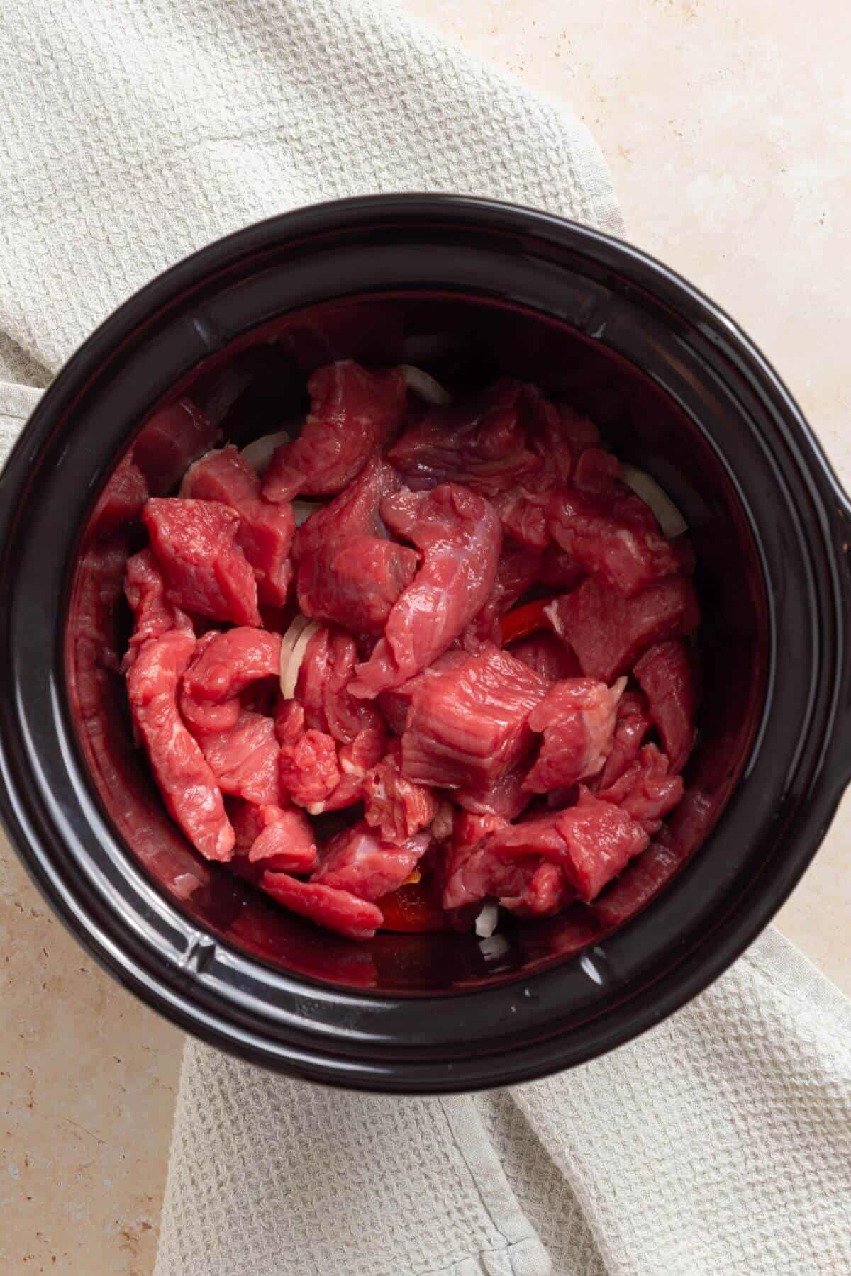 A crock pot filled with beef and onions.