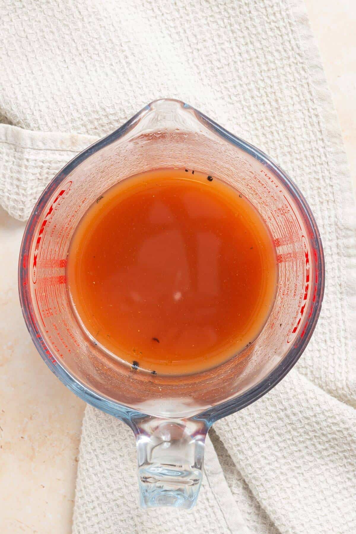 A glass measuring cup with a beef broth mixture in it.