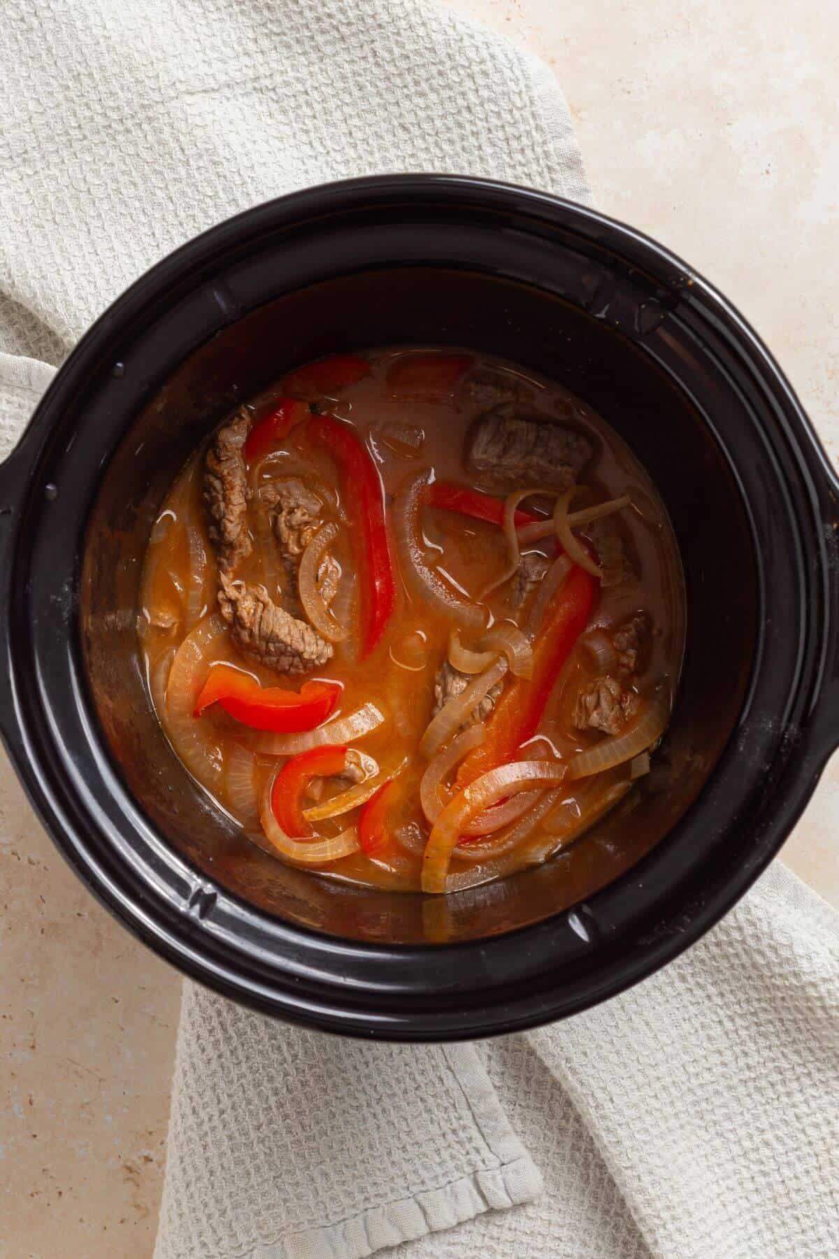 A crock pot with pepper steak in it.