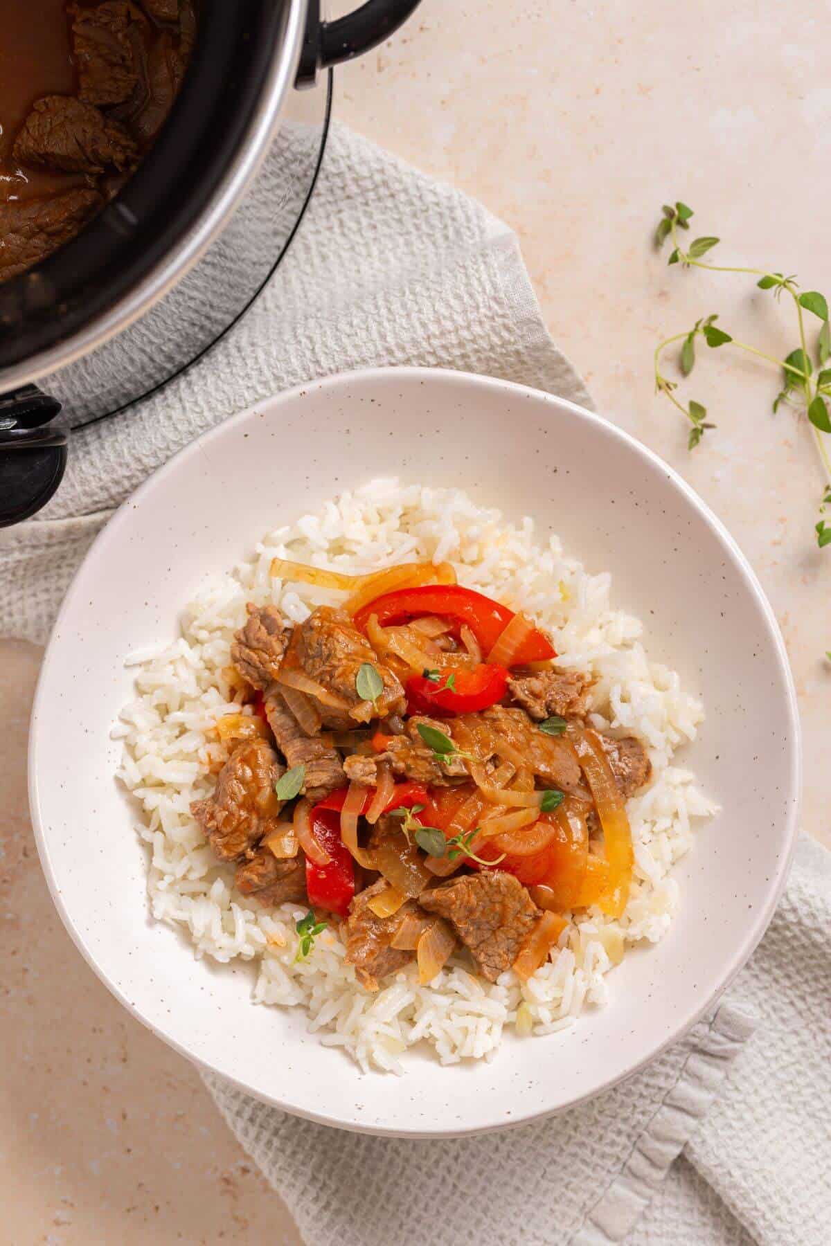 A bowl of rice with slow cooker pepper steak over it.