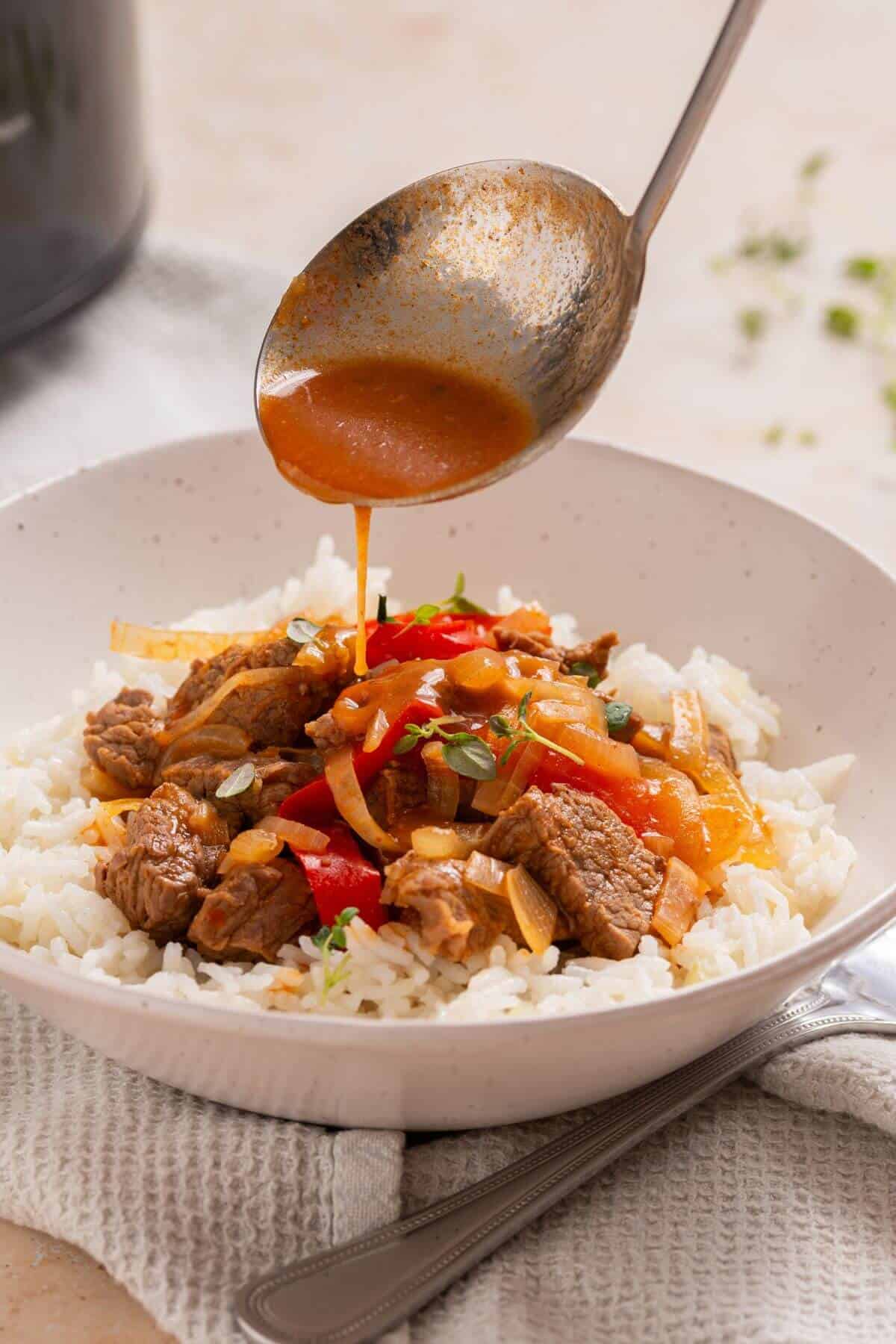 A spoon is being used to pour sauce over pepper steak on rice.