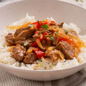 A bowl of rice with pepper steak over it.