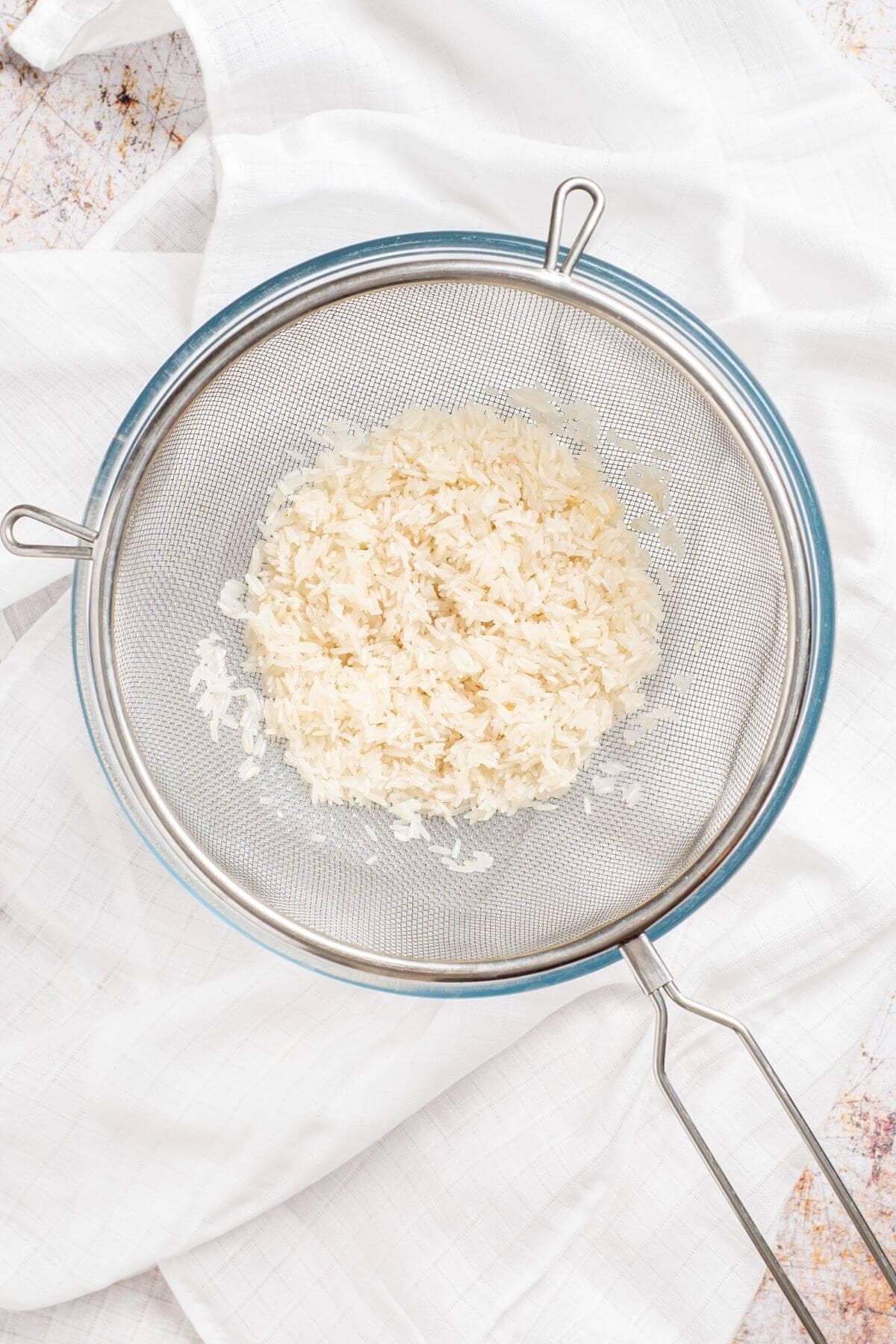 Rice in a strainer on a white cloth.