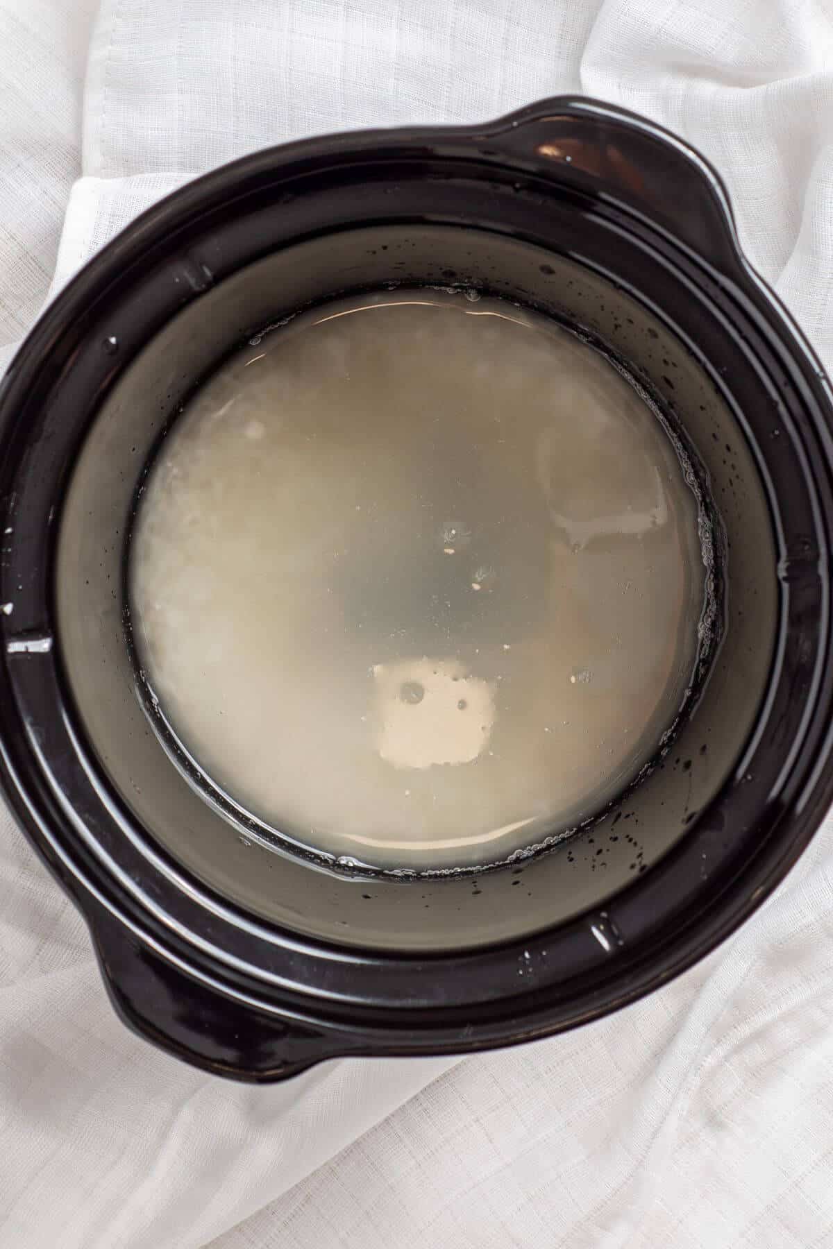 A crock pot filled with water and rice on top of a white sheet.