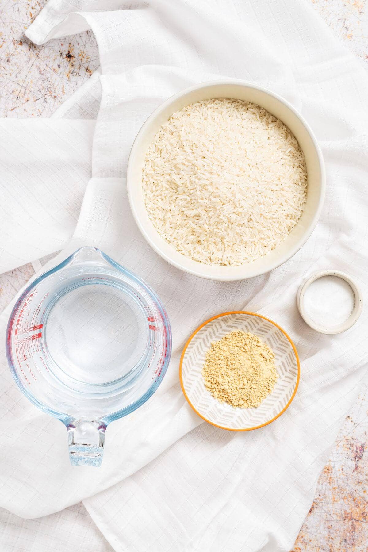 A bowl of rice and a measuring cup with water on a white cloth.
