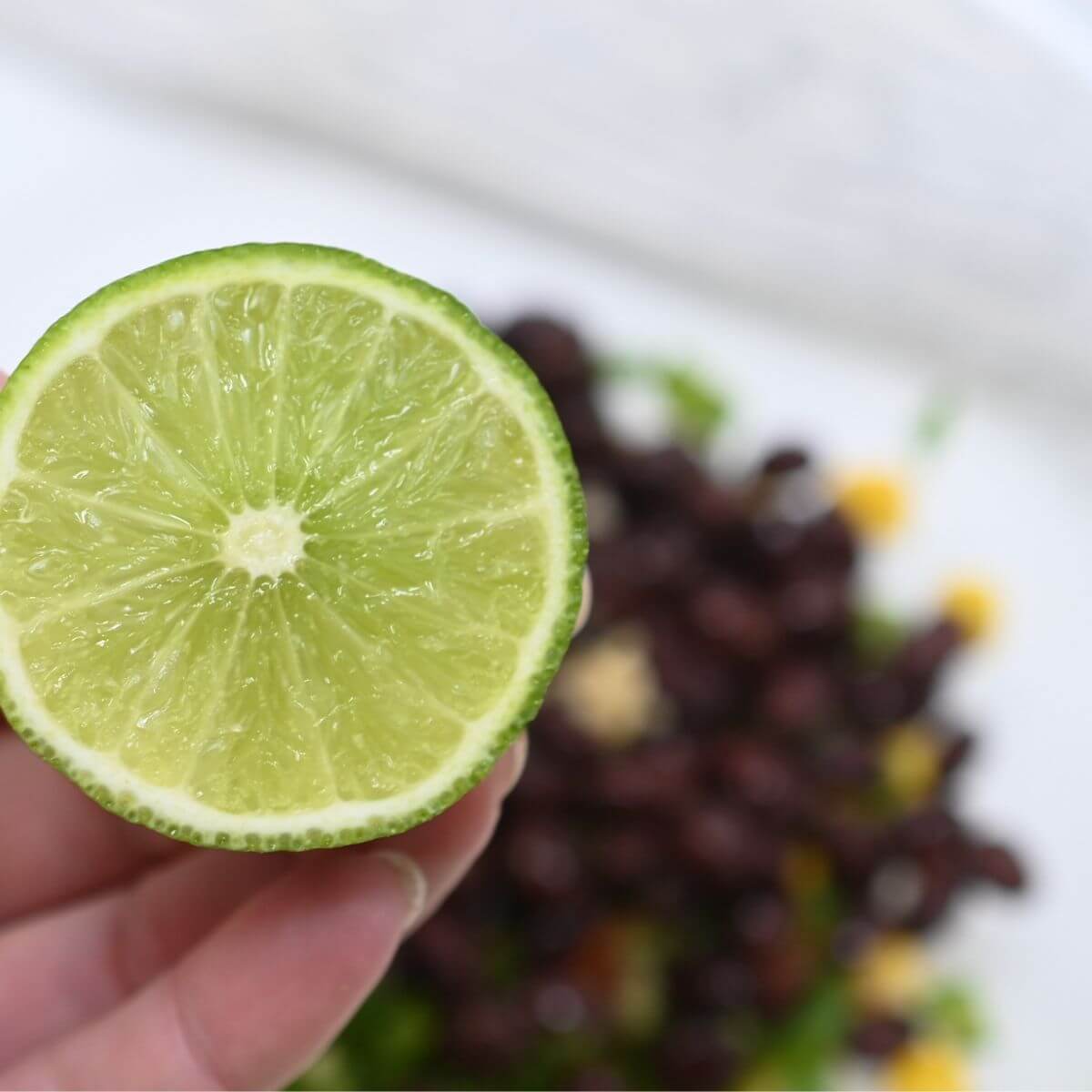 A hand holding a slice of lime over bowl with black beans and corn.