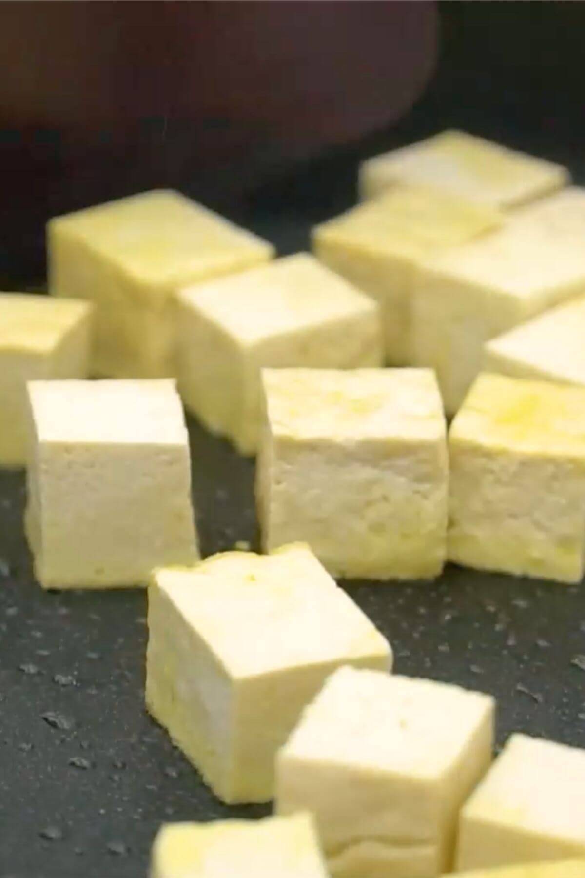 Tofu cubes are being cooked in a pan.