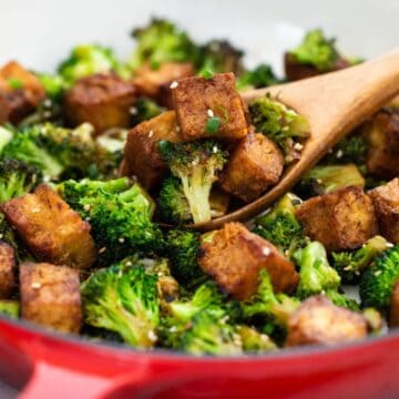 Tofu and broccoli in a pan with a wooden spoon.